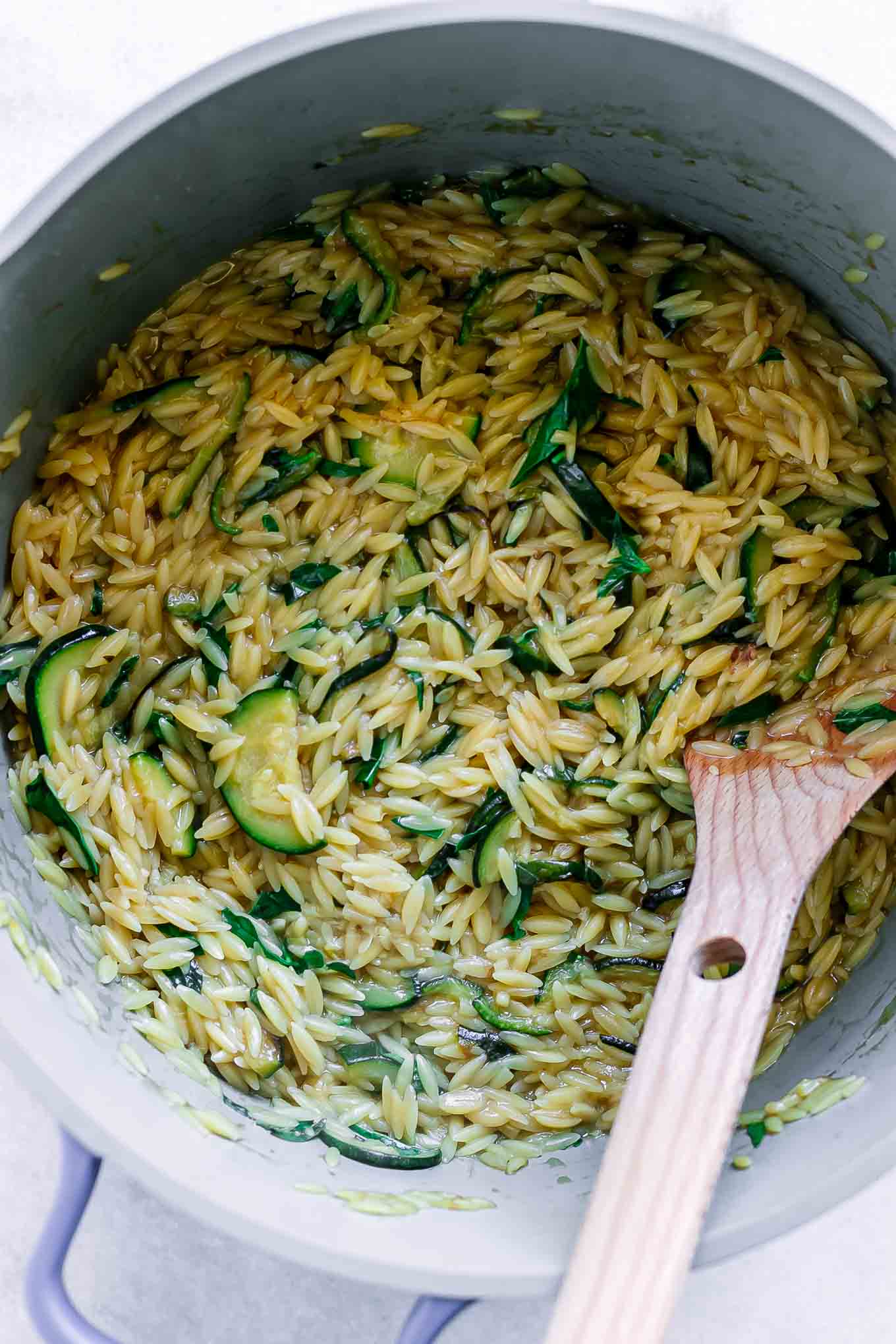 cooked orzo pasta in a pot with zucchini and a wood spoon