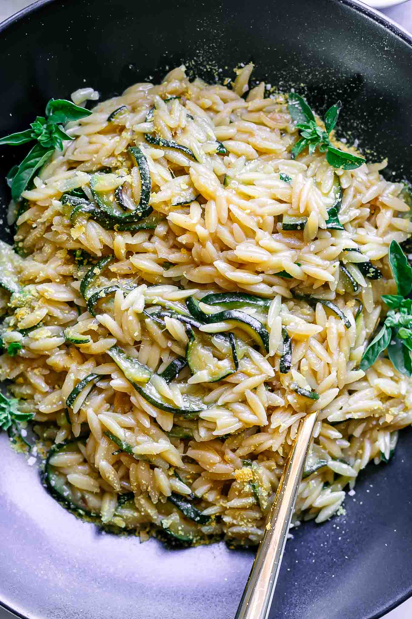 a close up photo of orzo with zucchini and basil in a black bowl