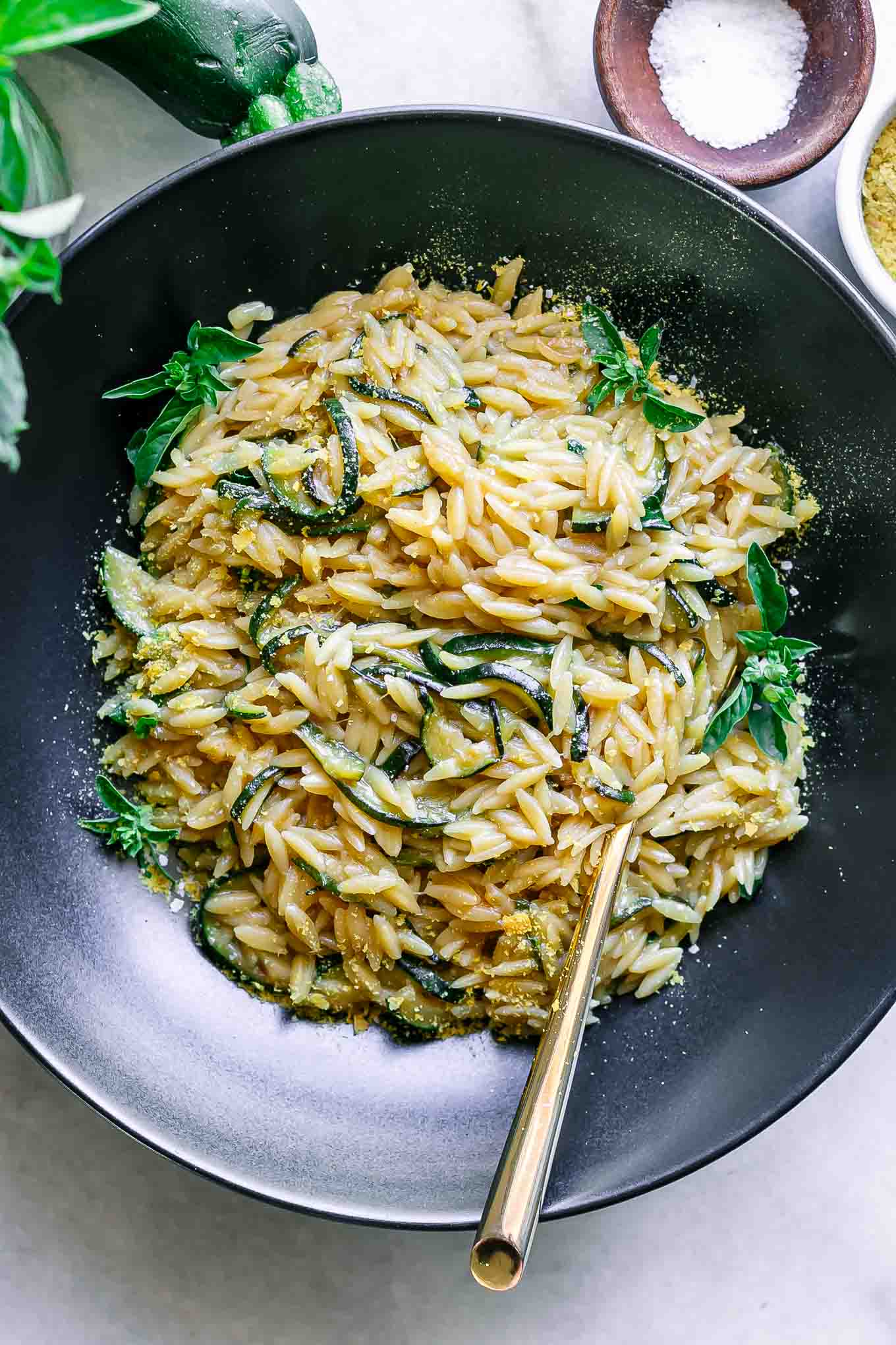 a black bowl with zucchini orzotto pasta with a gold fork on a white table