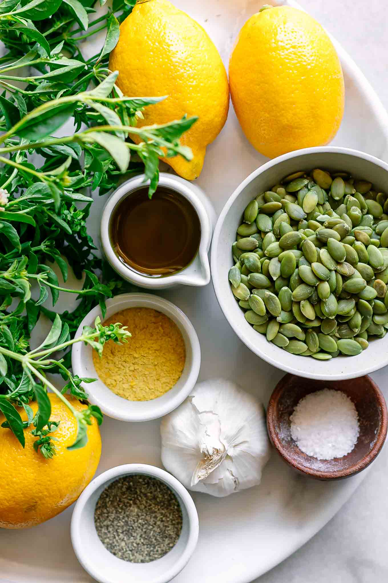 bowls of nuts, fresh basil, lemons, olive oil, garlic, salt, and pepper on a table for pesto