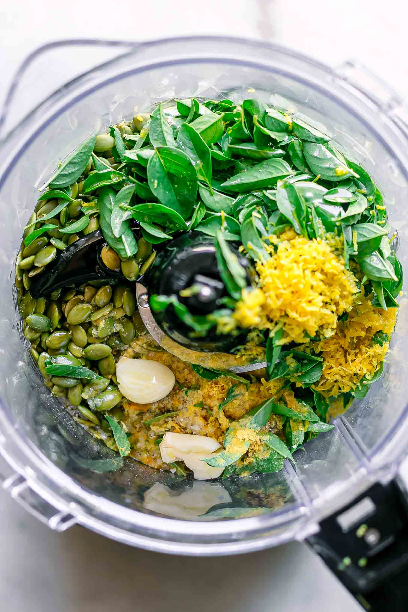 fresh basil, lemon zest, lemon juice, nuts, cheese, and other ingredients for pesto in a food processor before blending