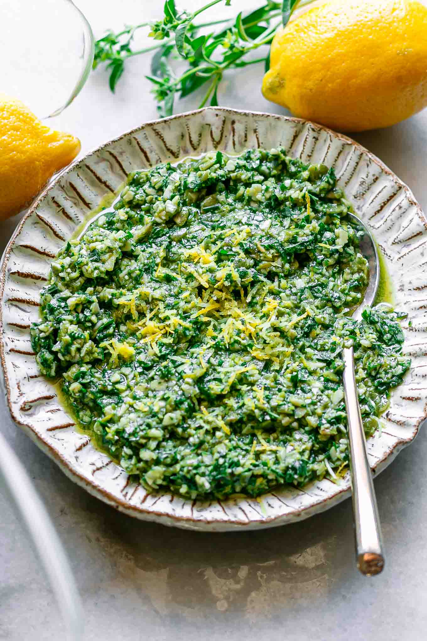 a white plate with lemon basil pesto and fresh lemons on a white table