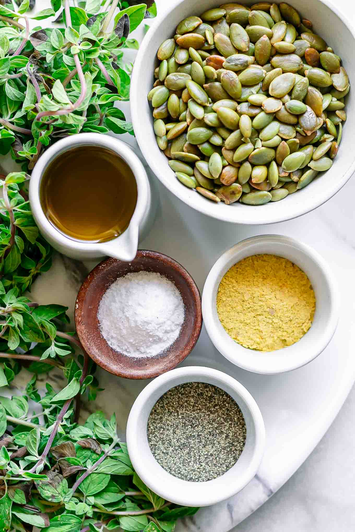 bowls of pumpkin seeds, cheese, olive oil, salt, pepper, garlic, and fresh oregano for pesto