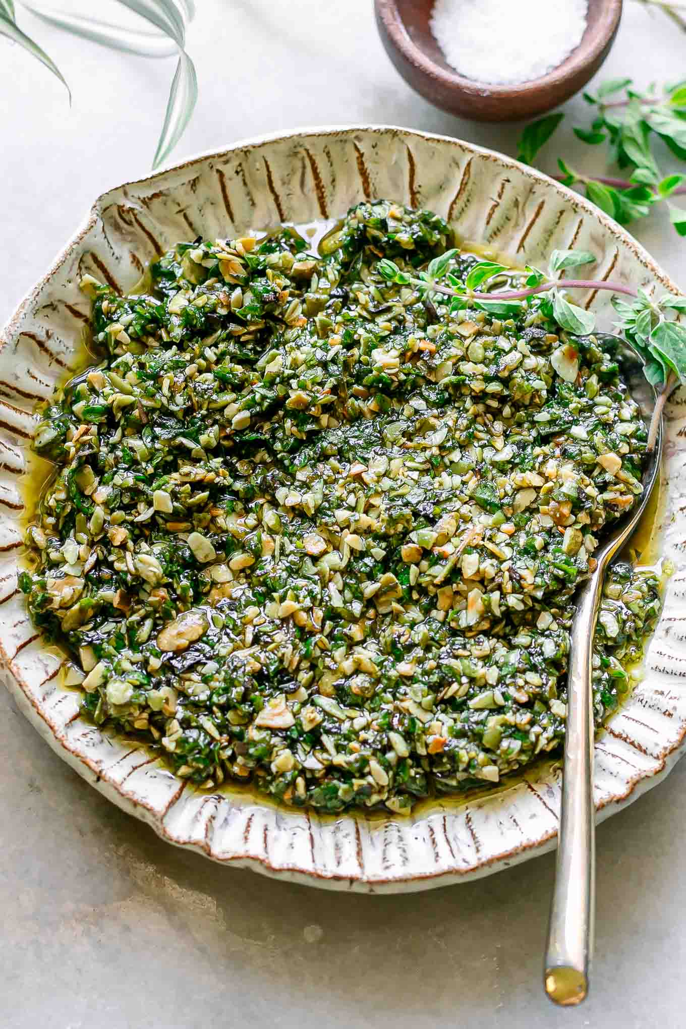 a bowl of oregano pesto on a white table with a gold spoon