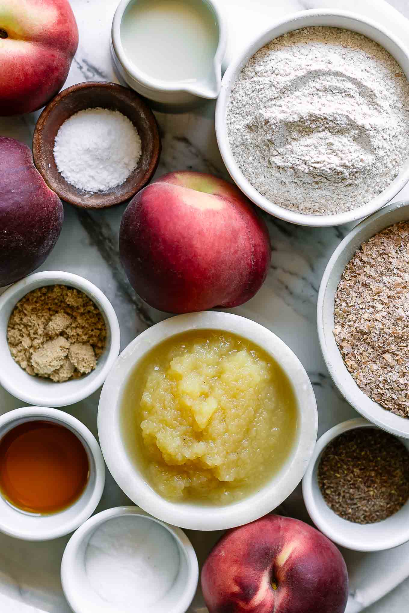 bowls of wheat bran, flour, peaches, applesauce, and other ingredients for peach bran muffins