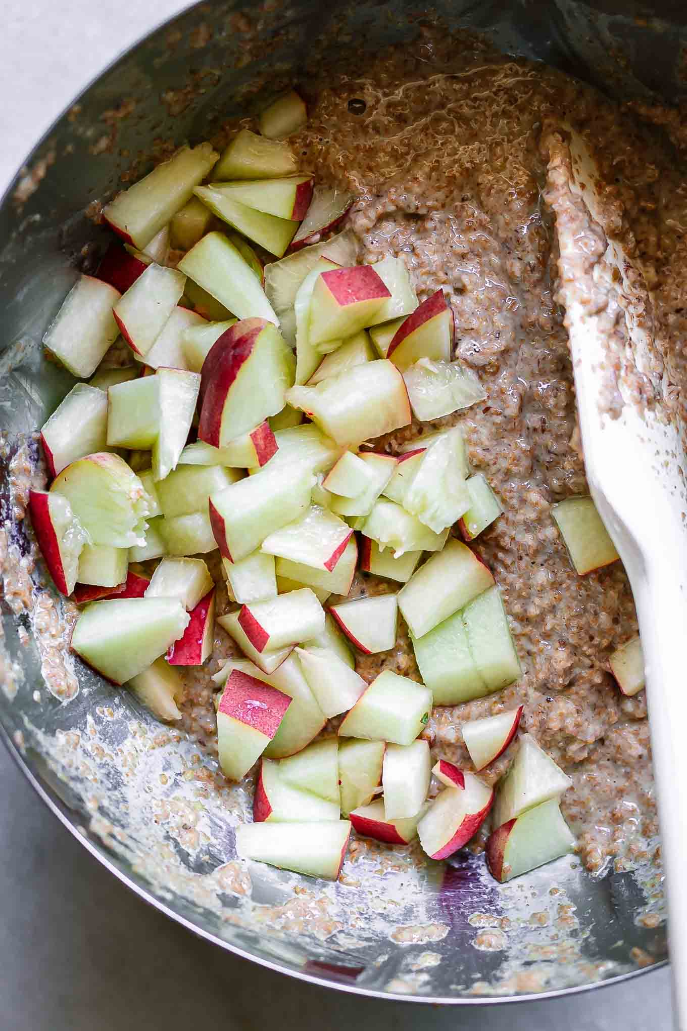 a white baking spatula folding peaches into bran muffin batter