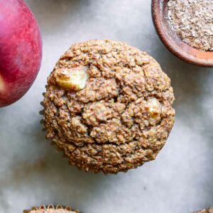 peach bran muffins on a white countertop with peaches and a bowl of wheat bran