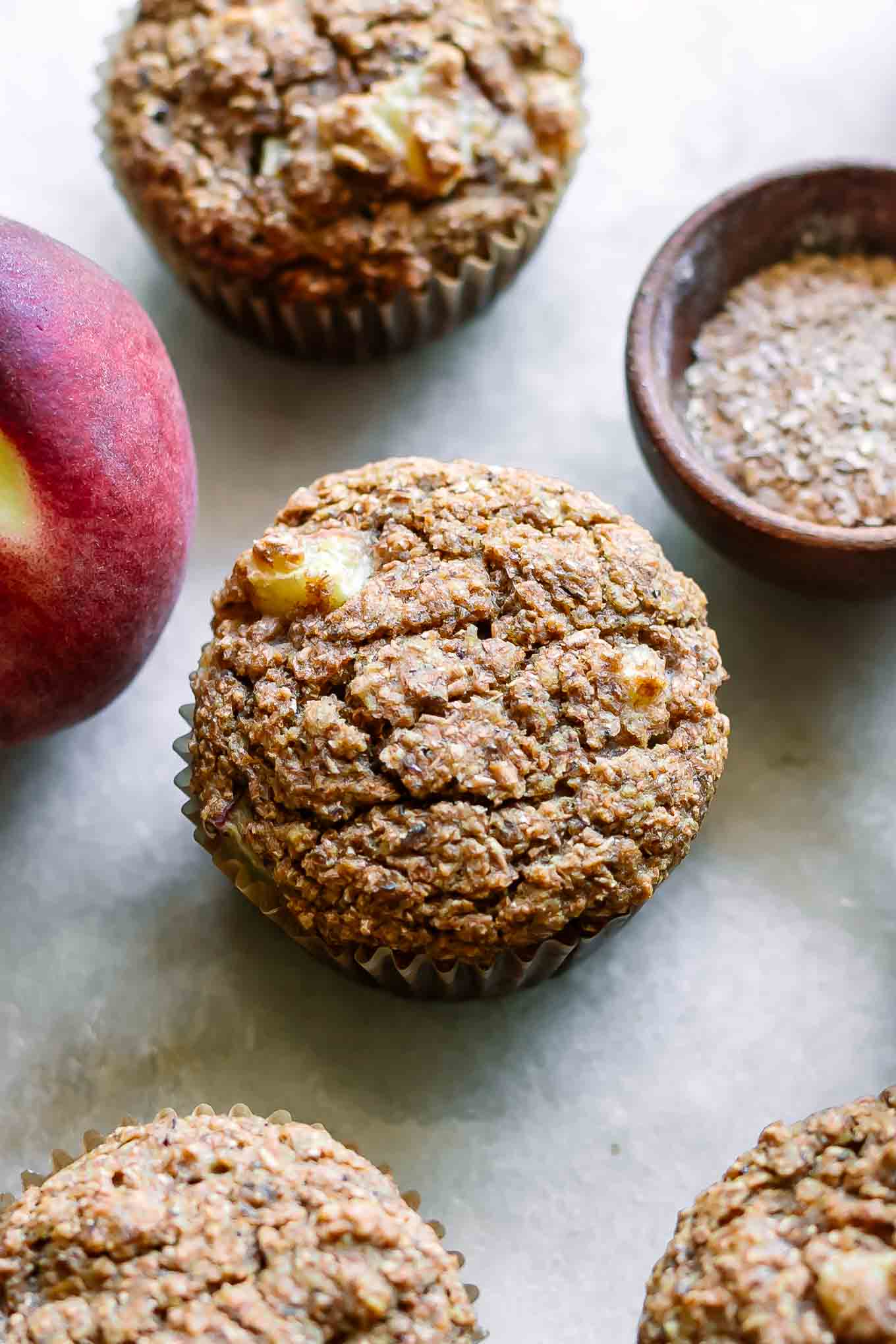 bran muffins with peaches on a white table with peaches and a bowl of wheat bran