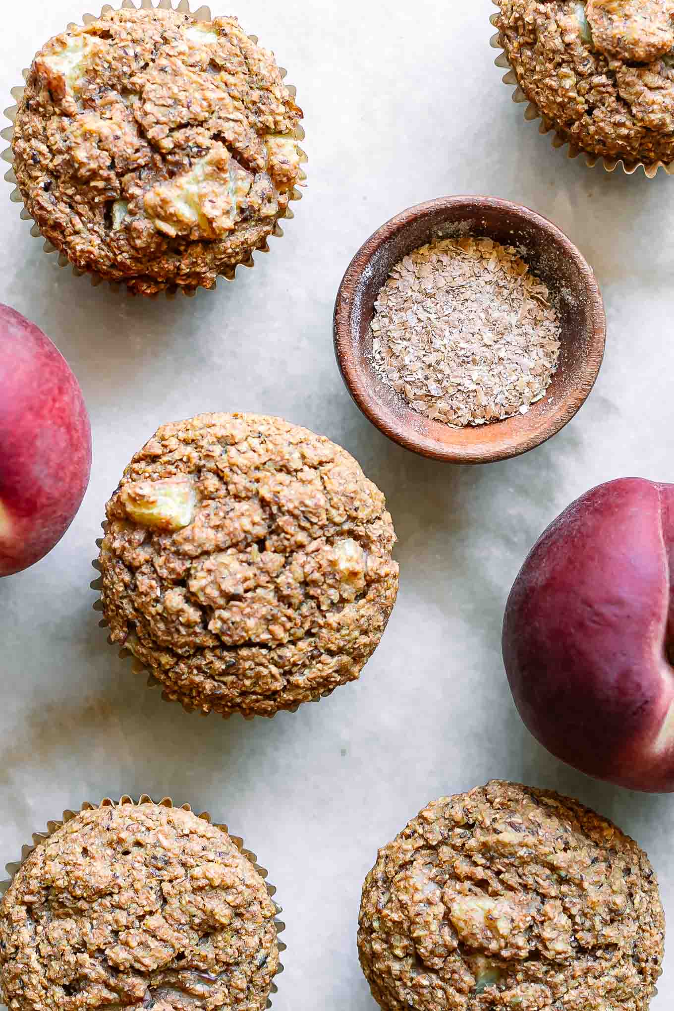 peach bran muffins on a white table with fresh peaches