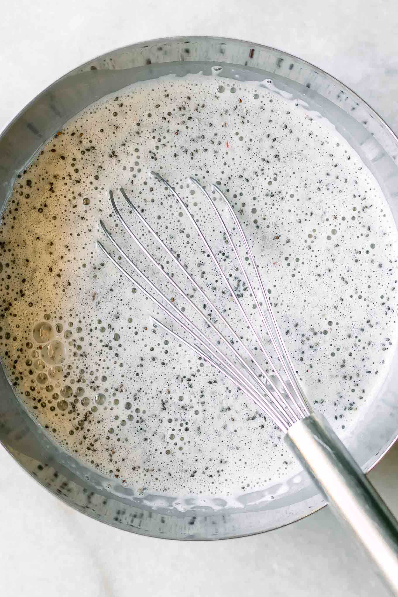 a mixing bowl with peach-flavored milk and chia seeds and a metal whisk