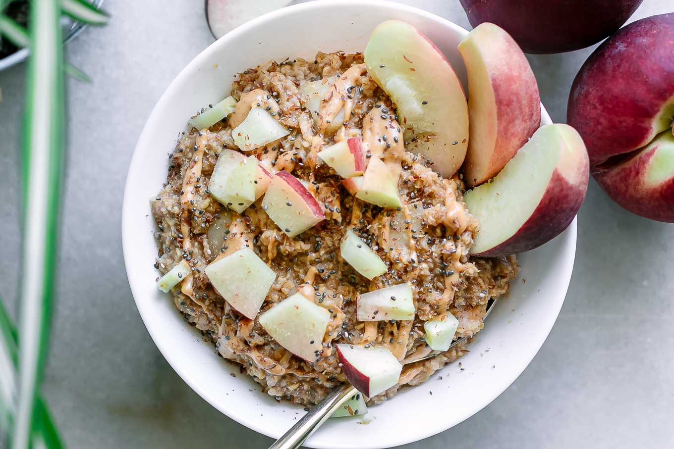 a bowl of peach oatmeal with chopped peaches and drizzled nut butter on top on a table with fresh peaches