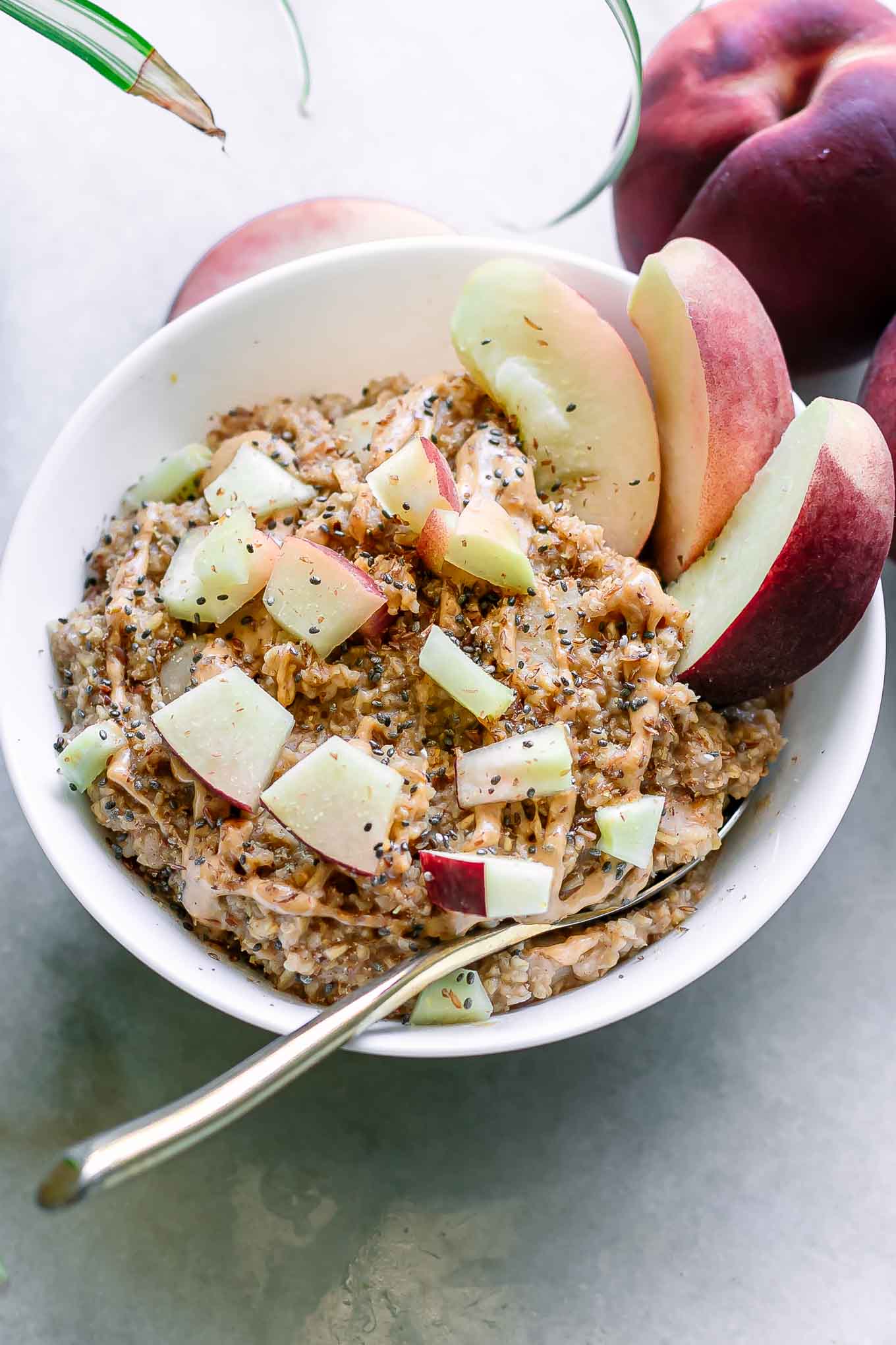 a bowl of peach oatmeal bowl on a white table with a gold fork