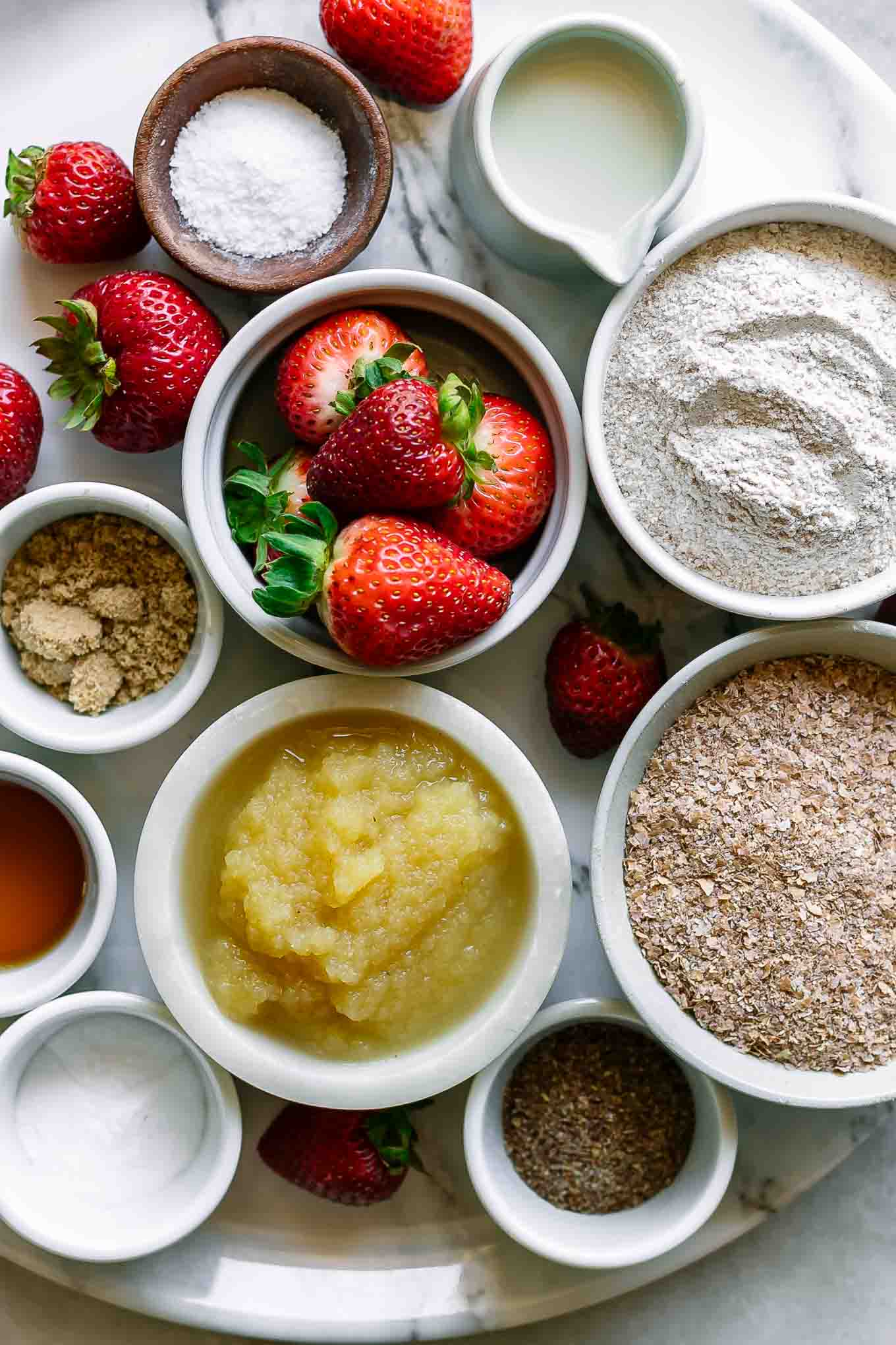 bowls of flour, wheat bran, applesauce, strawberries, and other ingredients for bran muffins