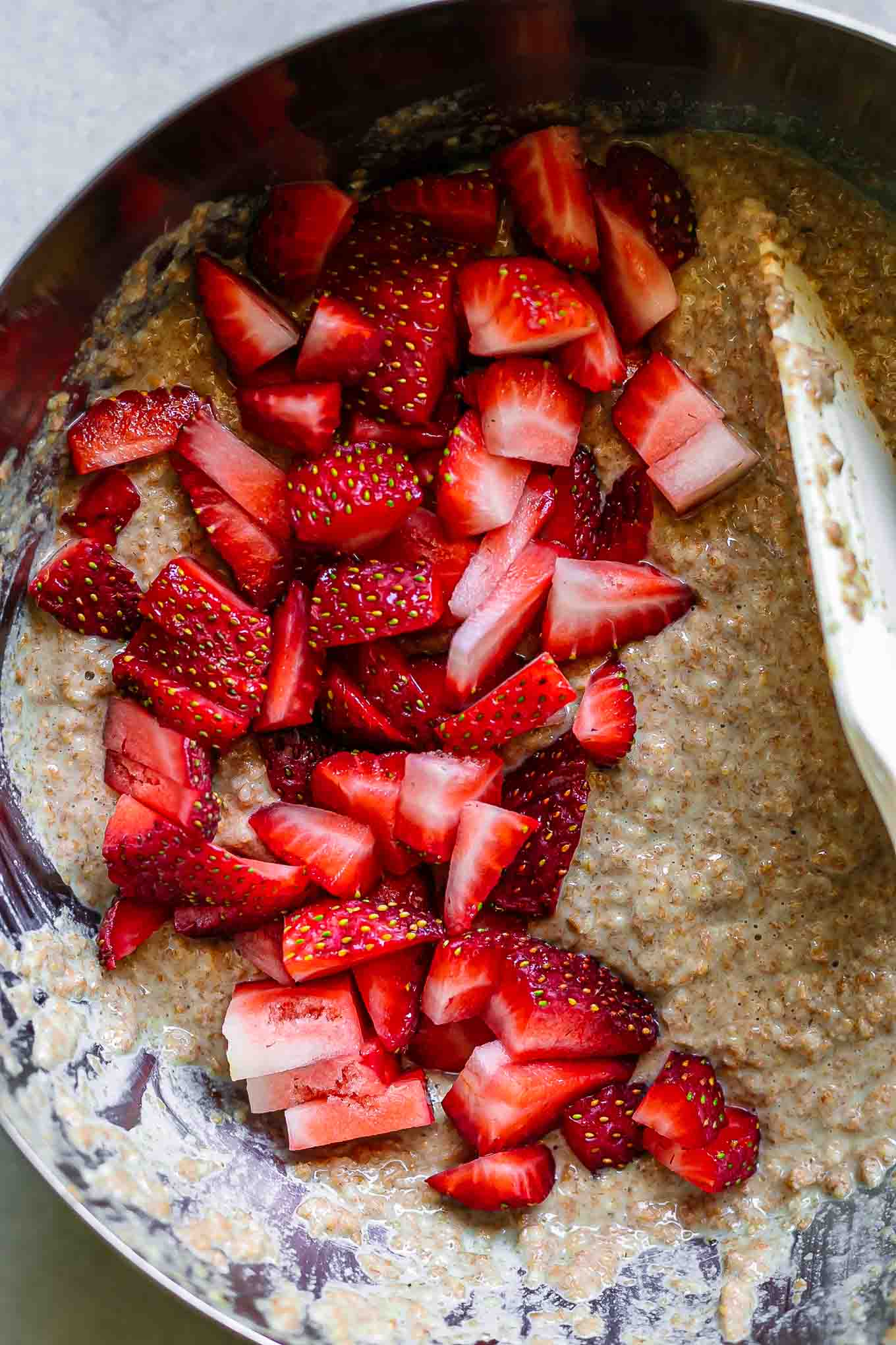 cut strawberries folding into a bran muffin batter with a white spatula