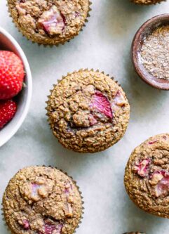 strawberry bran muffins on a white table with a bowl of strawberries and a bowl of wheat bran