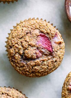 a strawberry bran muffin on a white table with a bowl of fresh strawberries