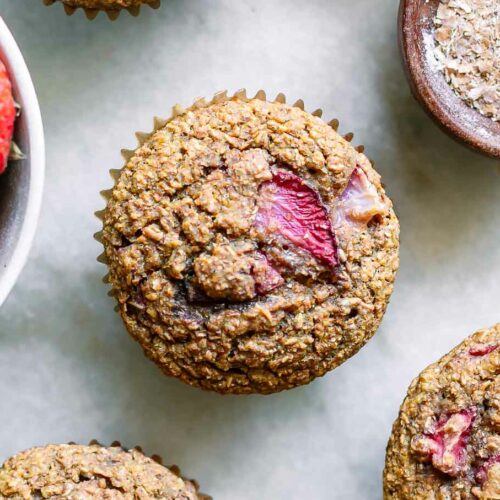 a strawberry bran muffin on a white table with a bowl of fresh strawberries