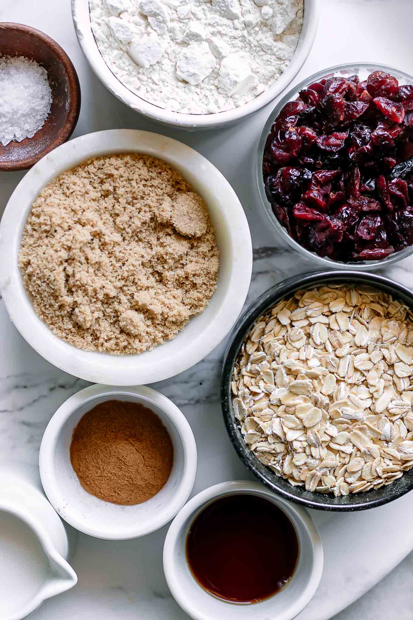 bowls of rolled oats, dried cranberries, flour, brown sugar, and other ingredients for oatmeal cookies