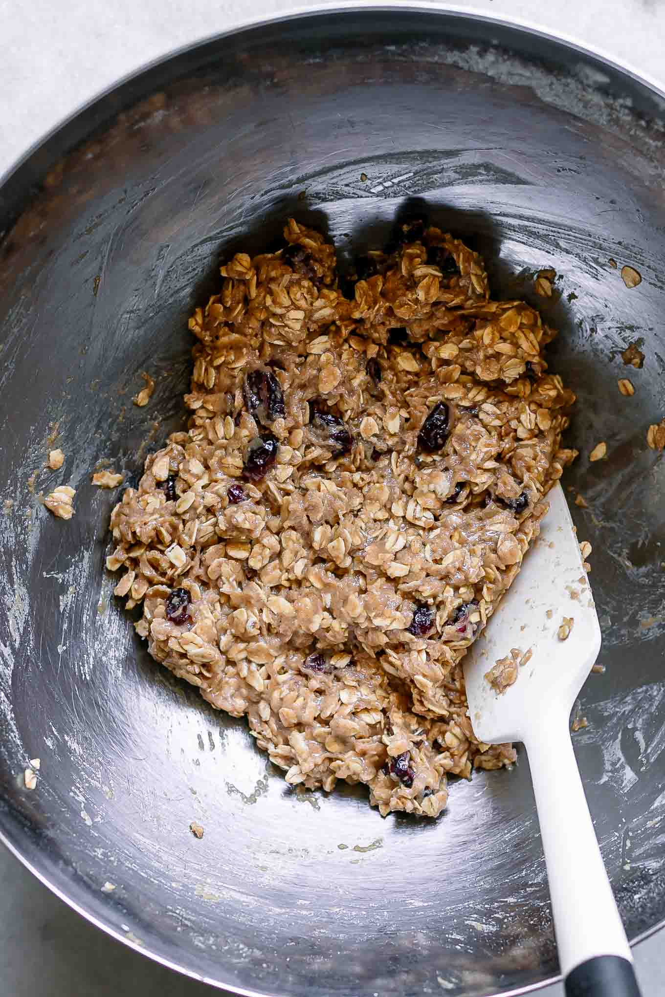 cranberry oatmeal cookie dough inside a metal bowl with a white baking spatula