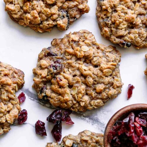 vegan cranberry oatmeal cookies on a white table with a bowl of dried cranberries