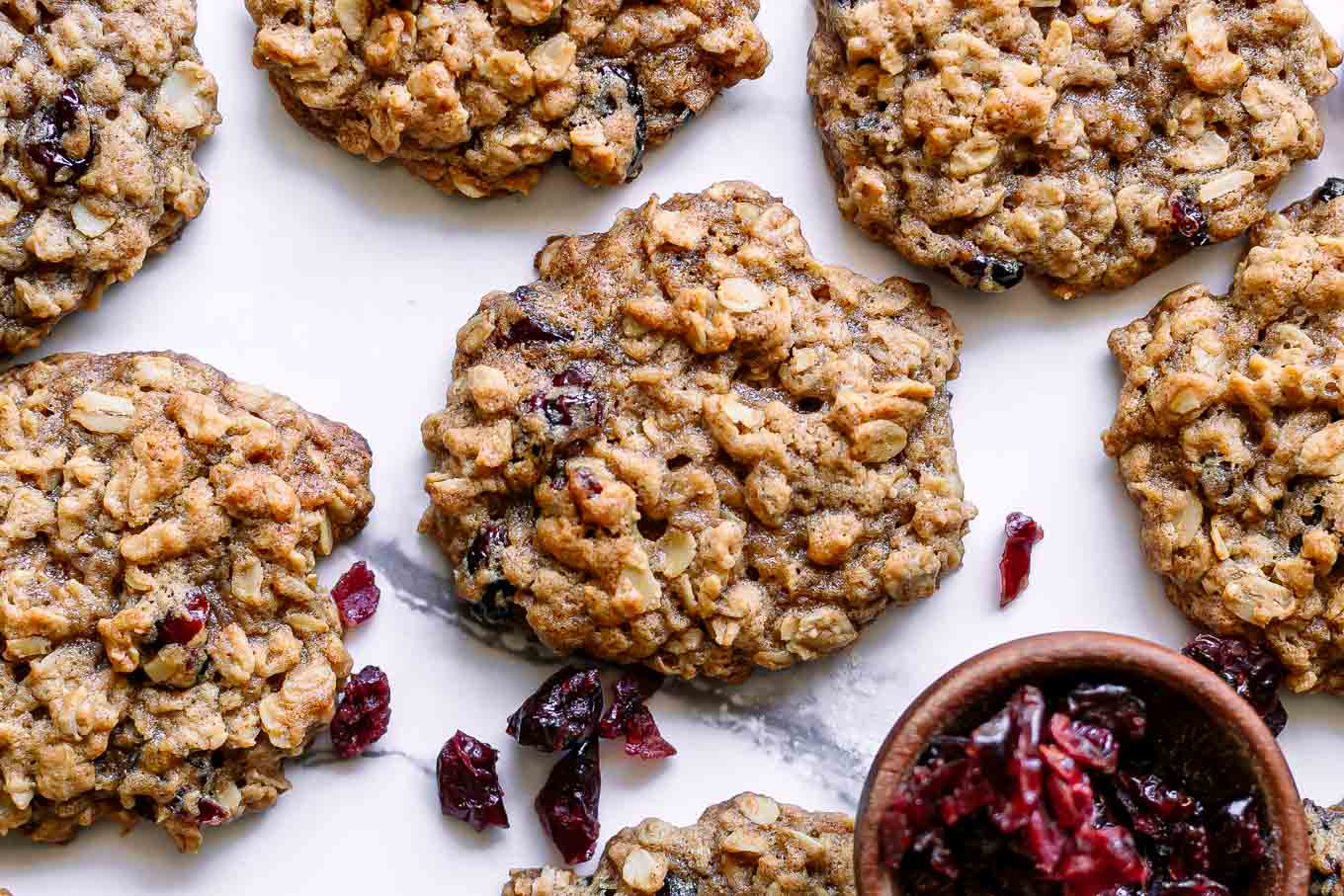 vegan cranberry oatmeal cookies on a white table with a bowl of dried cranberries
