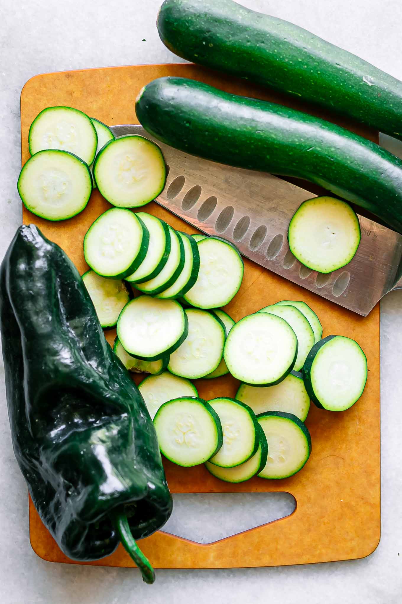 cut zucchini on a wood cutting board with a poblano pepper