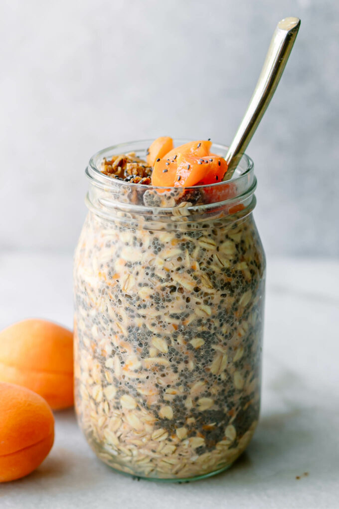 a mason jar with overnight oats with apricots on a white countertop with a gold spoon