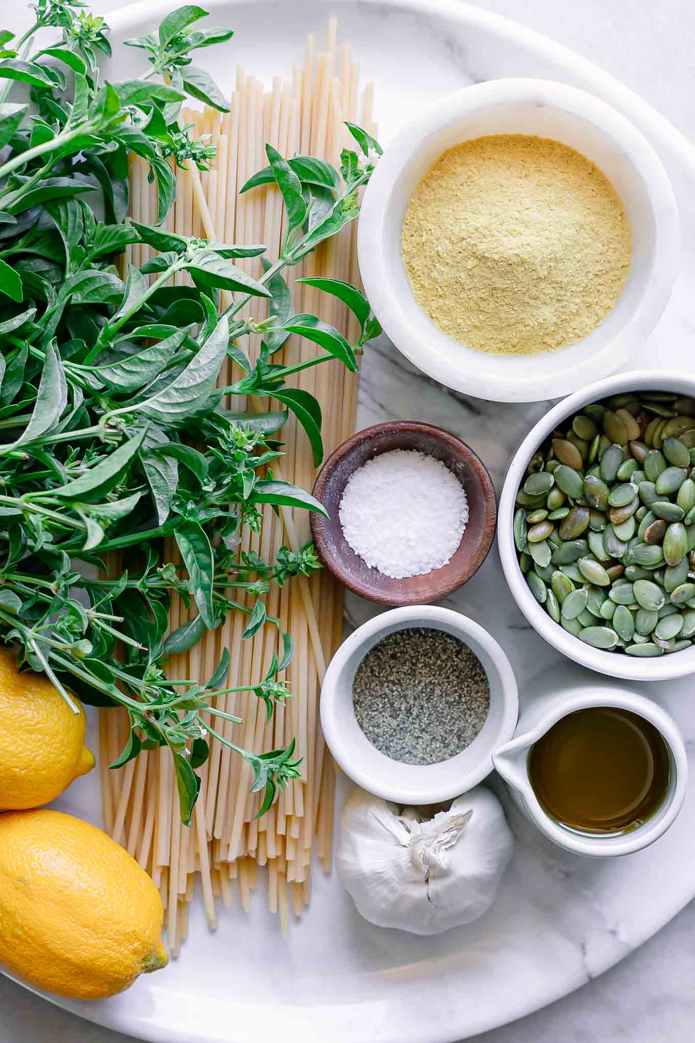 pasta, basil, lemons, nuts, and bowls of oils and spices for pesto pasta with lemons