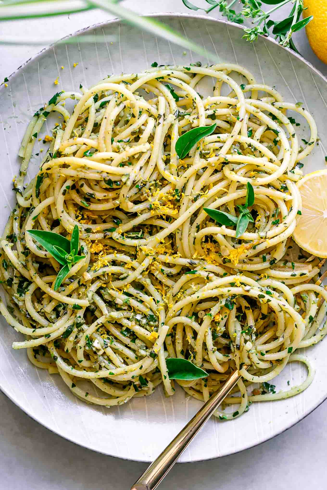 a white plate with lemon pesto pasta with fresh basil and a lemon as garnish