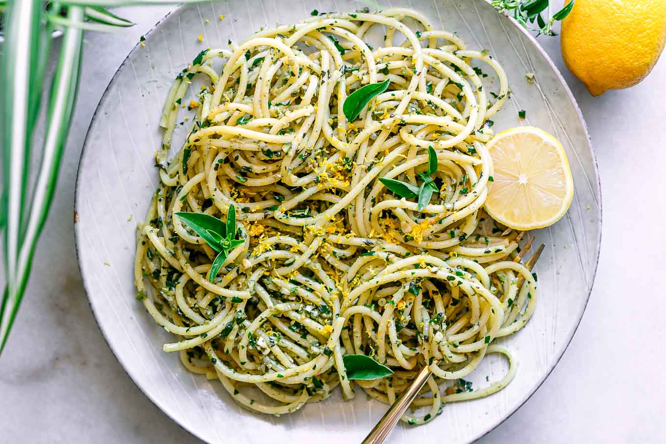 a white plate with lemon pesto pasta on a table with fresh lemons and fresh basil