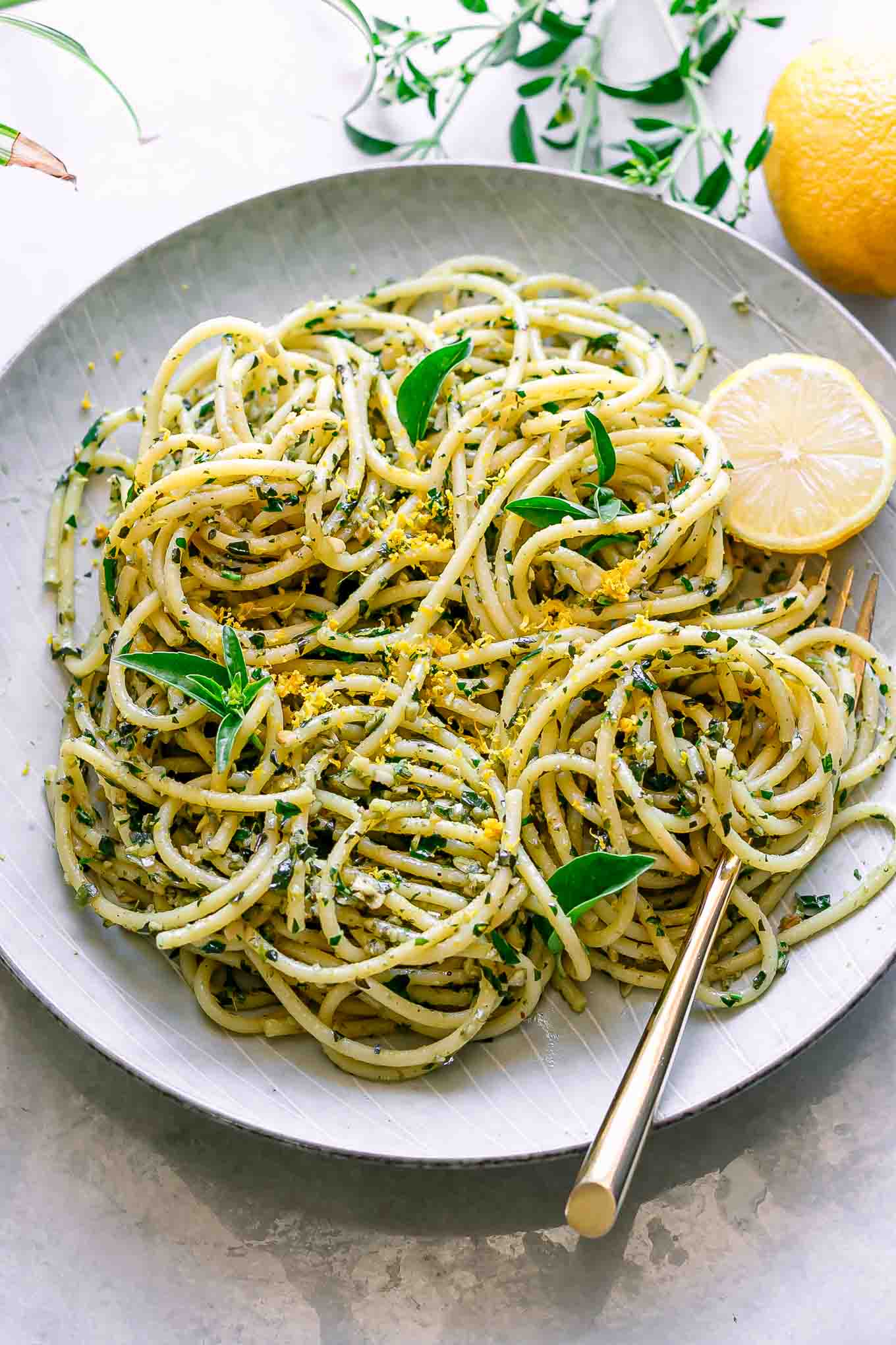 a plate of pesto pasta with lemon zest on a white table with a gold fork