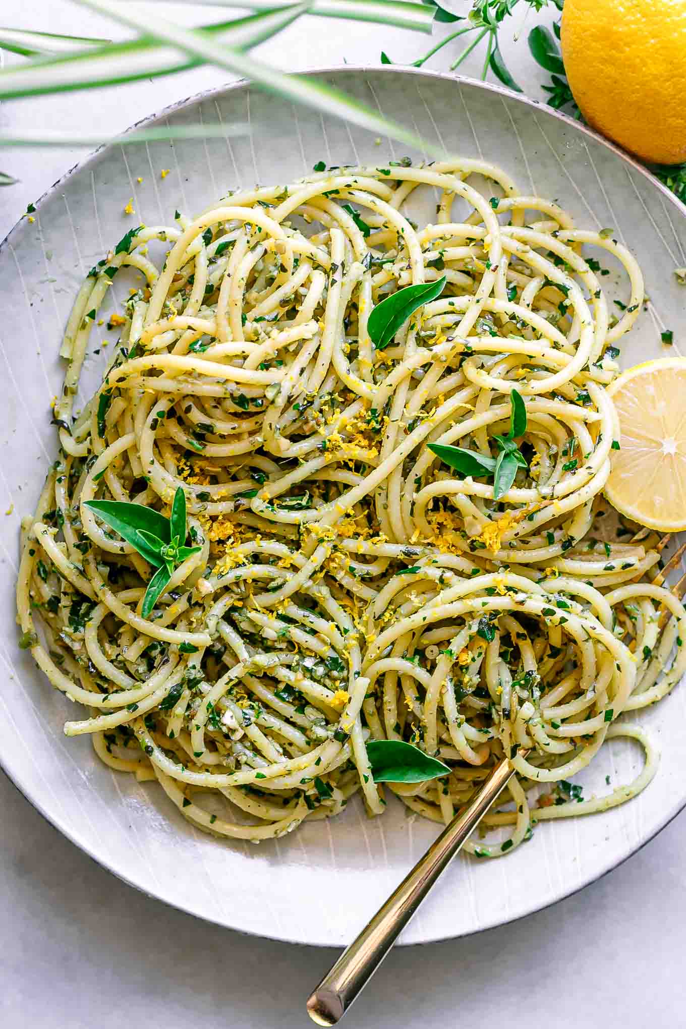 a plate of pasta with lemon pesto on a white table with fresh basil and a lemon