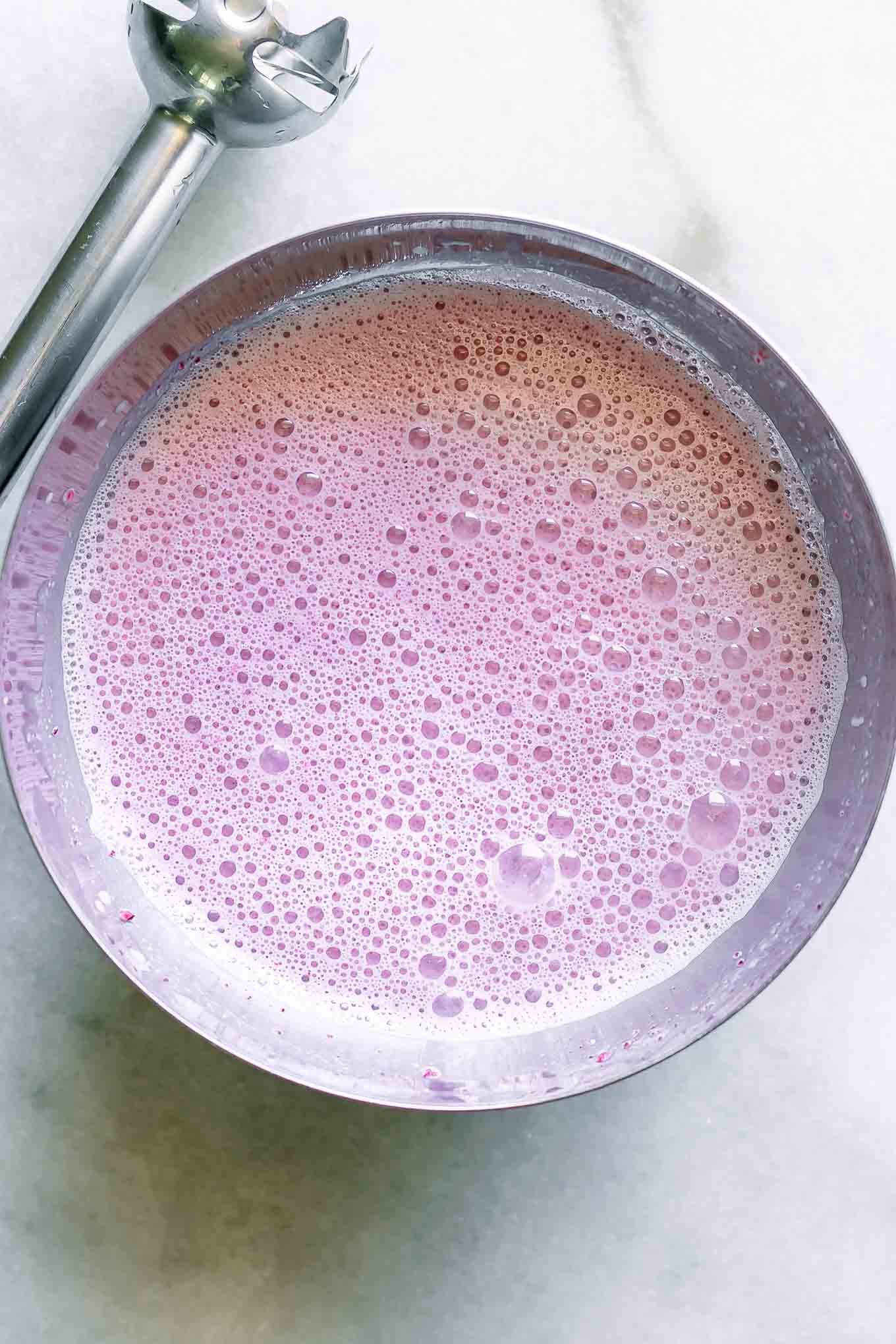 a bowl of purple plum-flavored milk on a table with an immersion blender