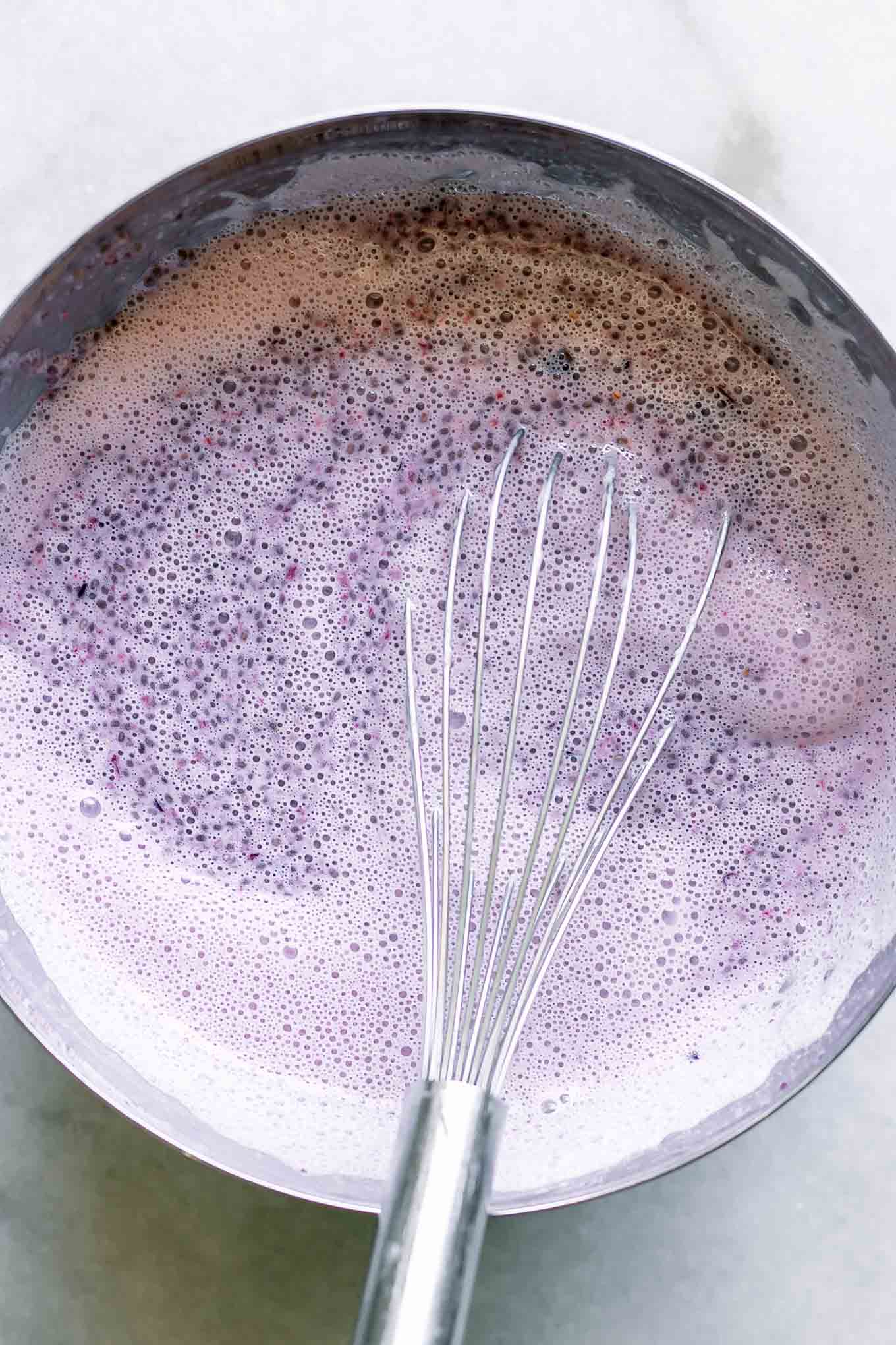 chia seeds in plum-flavored milk in a bowl with a whisk on a white table