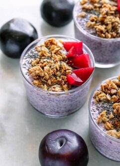 small jars of purple plum chia pudding on a table with fresh plums