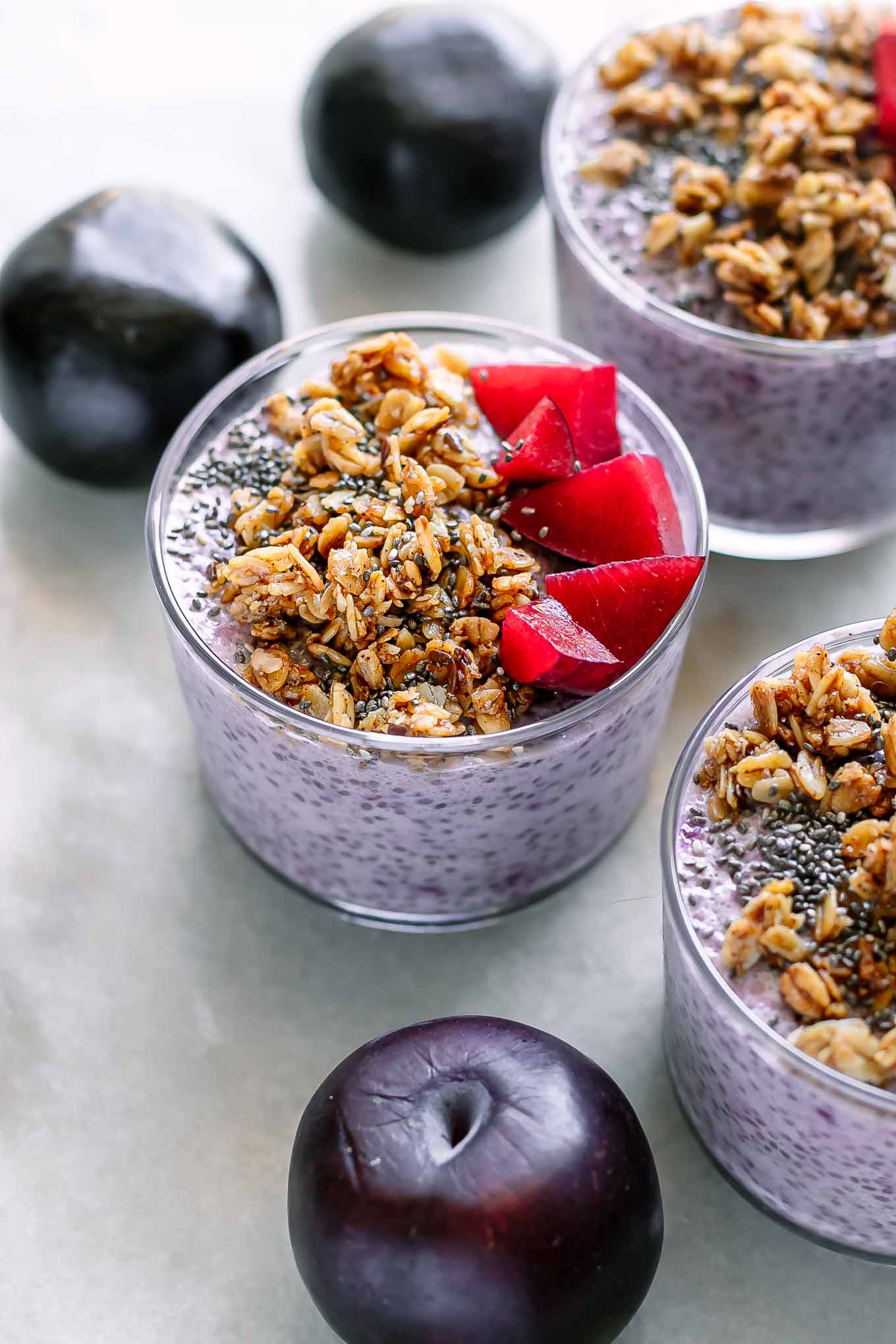 small jars of purple plum chia pudding on a table with fresh plums