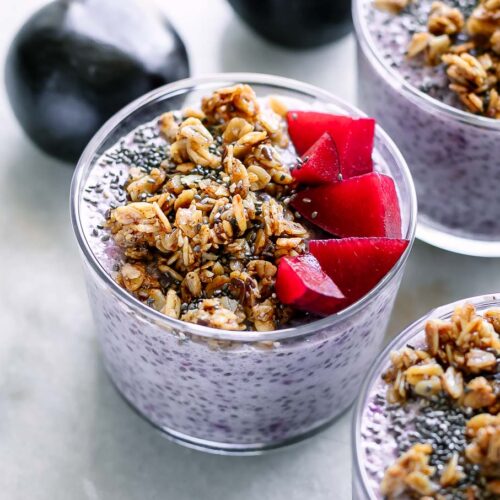bowls of plum chia pudding with granola on a white table with fresh plums