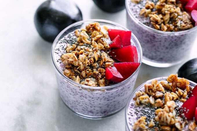 bowls of plum chia pudding with granola on a white table with fresh plums