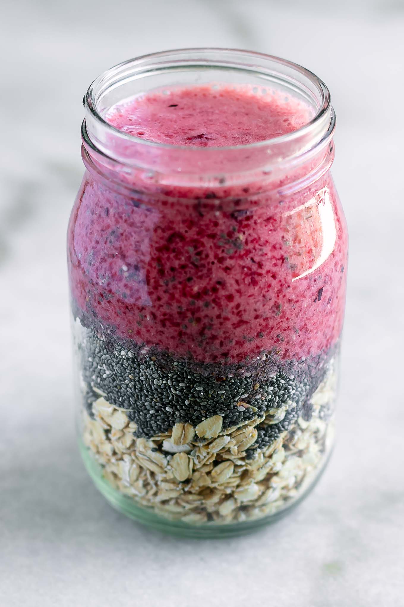 a mason jar with rolled oats, chia seeds, and purple plum-flavored milk on a white table
