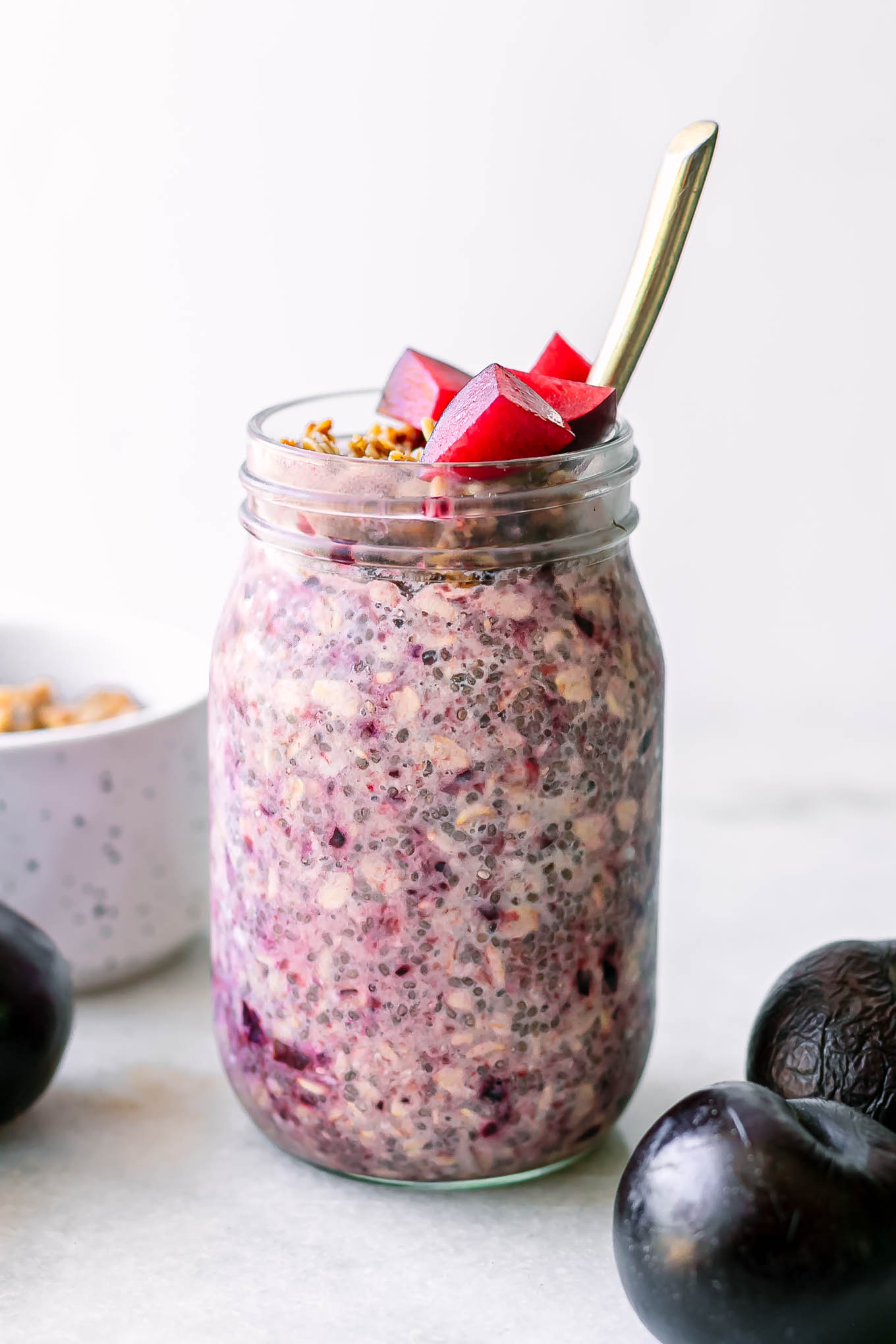 purple overnight oats with plums on top in a mason jar with a gold fork on a white table