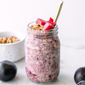 purple plum overnight oats in a jar with granola and cut plums as garnish on a white table