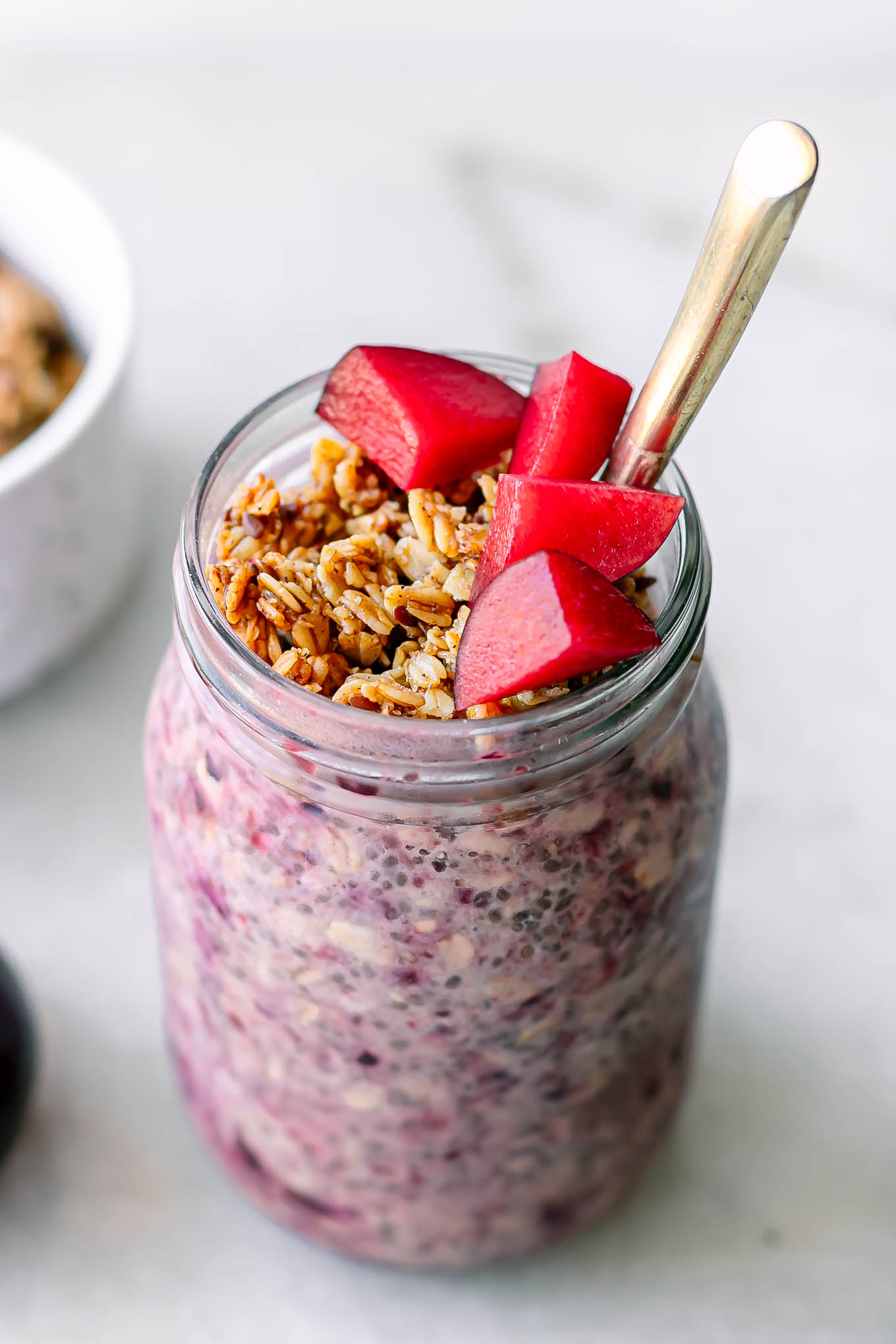 a jar with plum overnight oats garnished with granola and cut plums on a white table