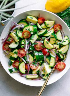 a zucchini and tomato salad with fresh basil in a white bowl and a gold fork