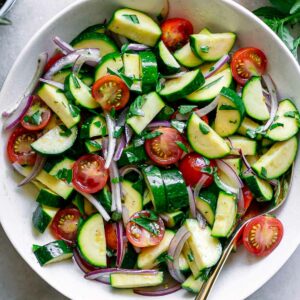 a raw zucchini tomato onion and basil salad in a white bowl on a white table with fresh basil
