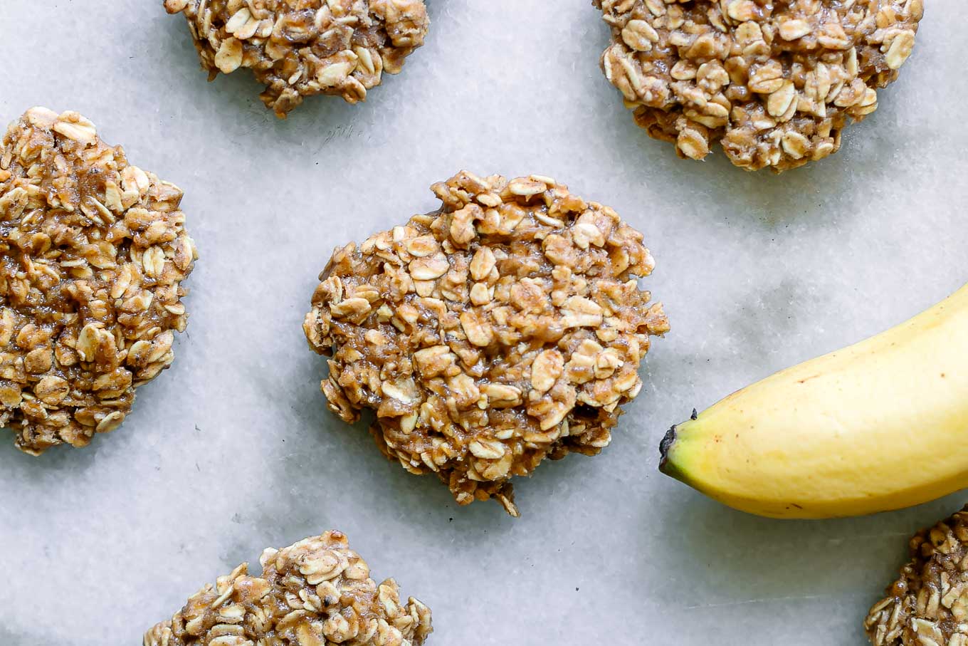 vegan banana oatmeal cookies on a white table with a yellow banana