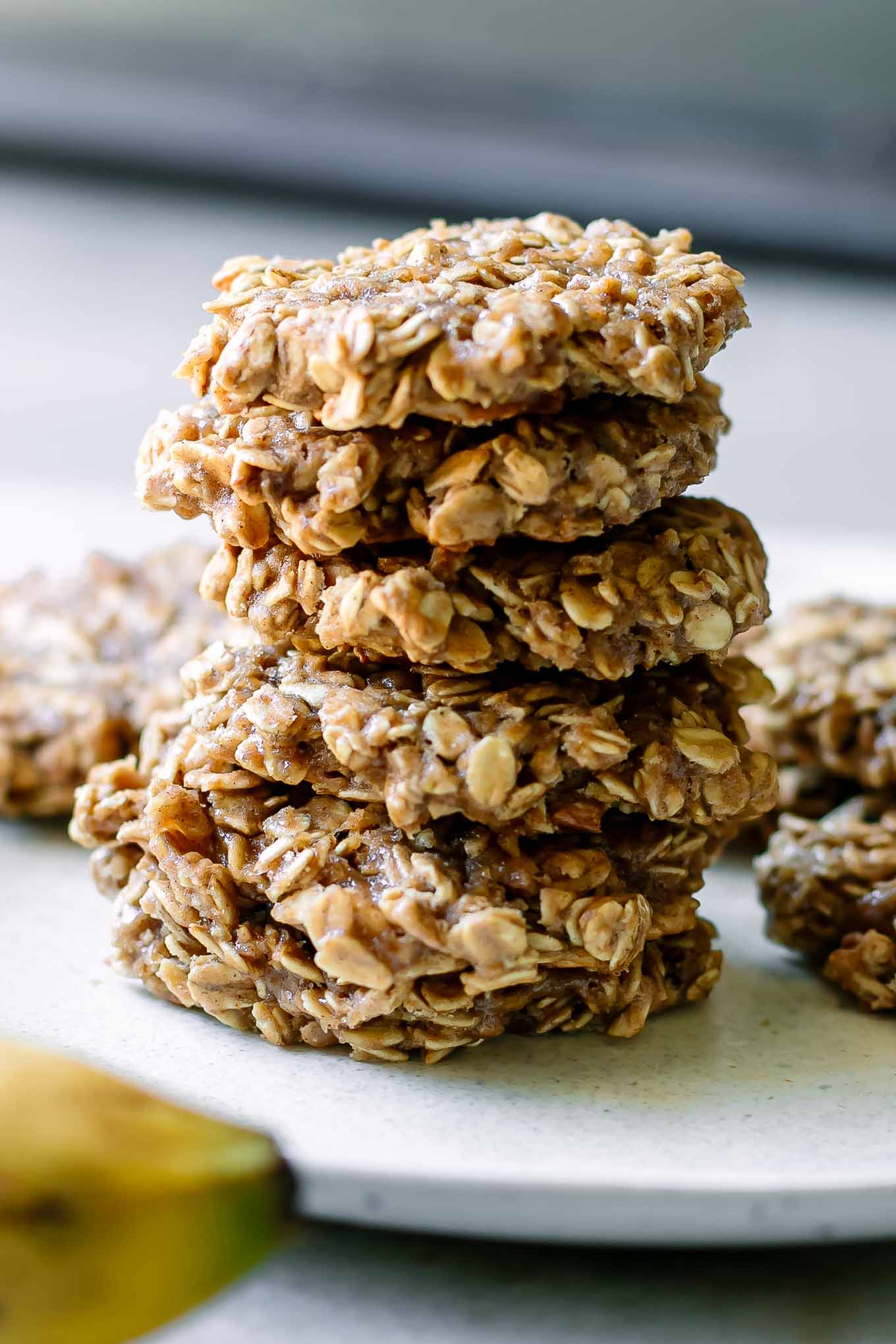 stacked oatmeal banana cookies on a white table with a fresh banana