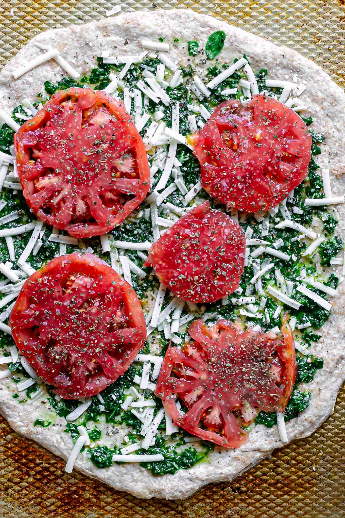 pizza dough with pesto, mozzarella cheese, and tomato slices on a baking sheet before baking