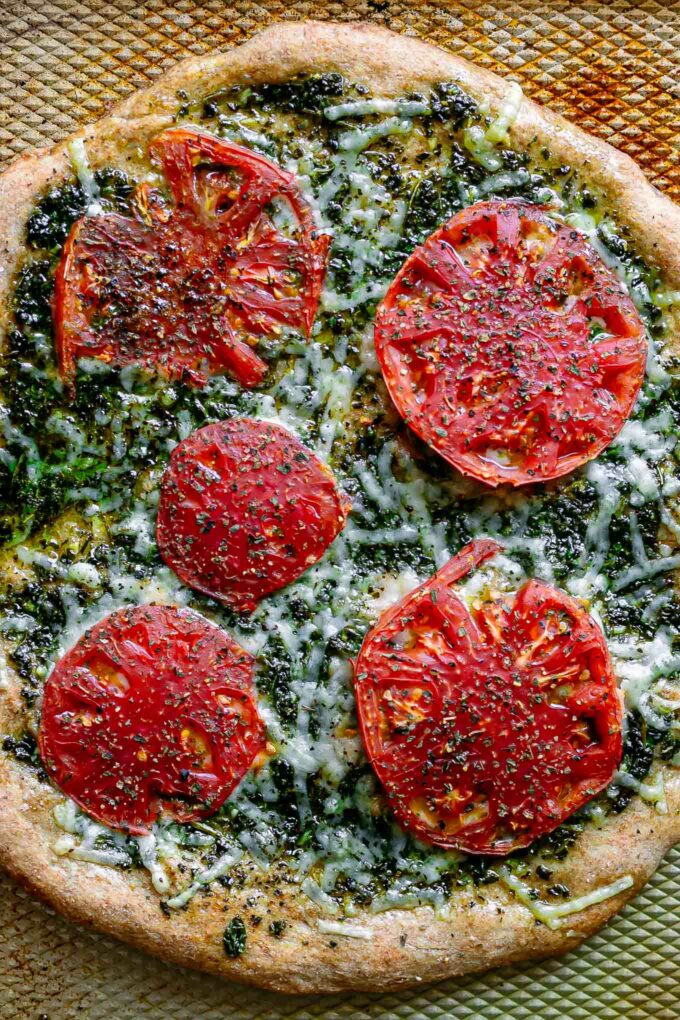 a pesto pizza with roasted tomatoes on a sheet pan after baking