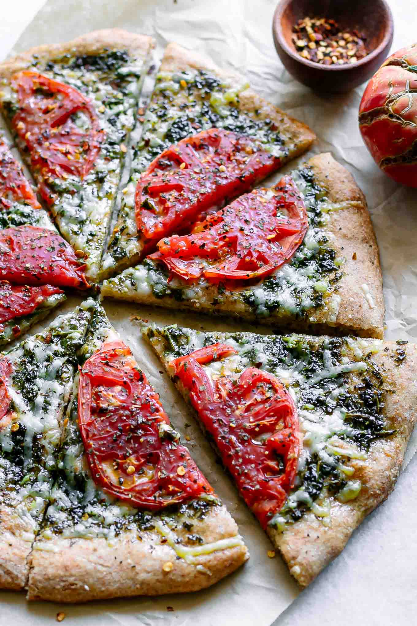 a pesto pizza with tomatoes cut into slices on a white table