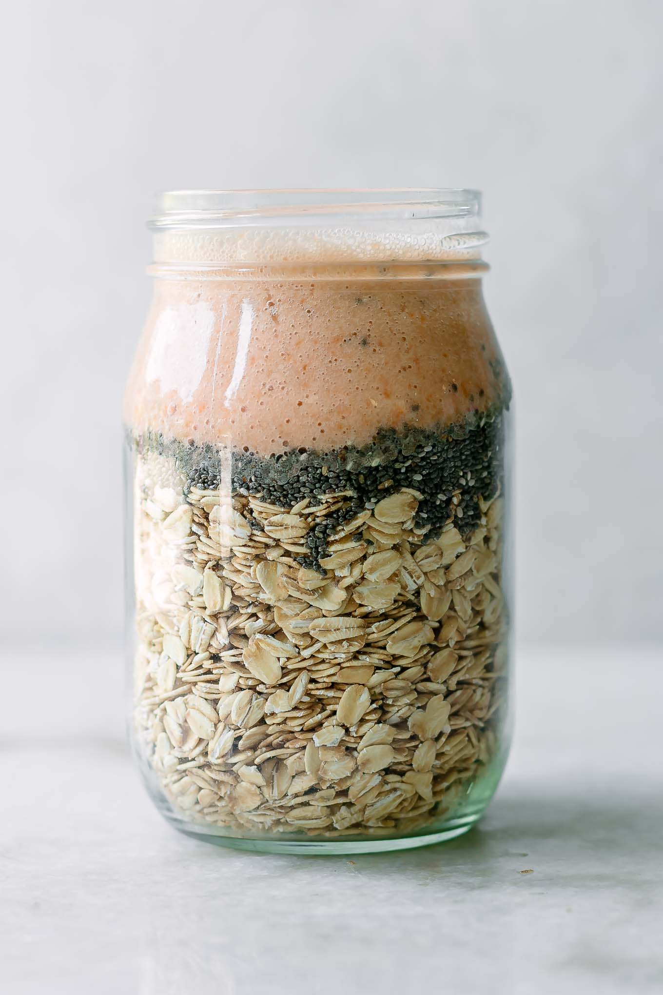 rolled oats, chia seeds, and apricot flavored milk in a mason jar on a white table